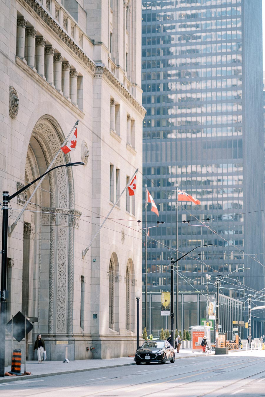 Downtown Toronto street view with historic architecture, Canadian flags, and a modern skyscraper backdrop.