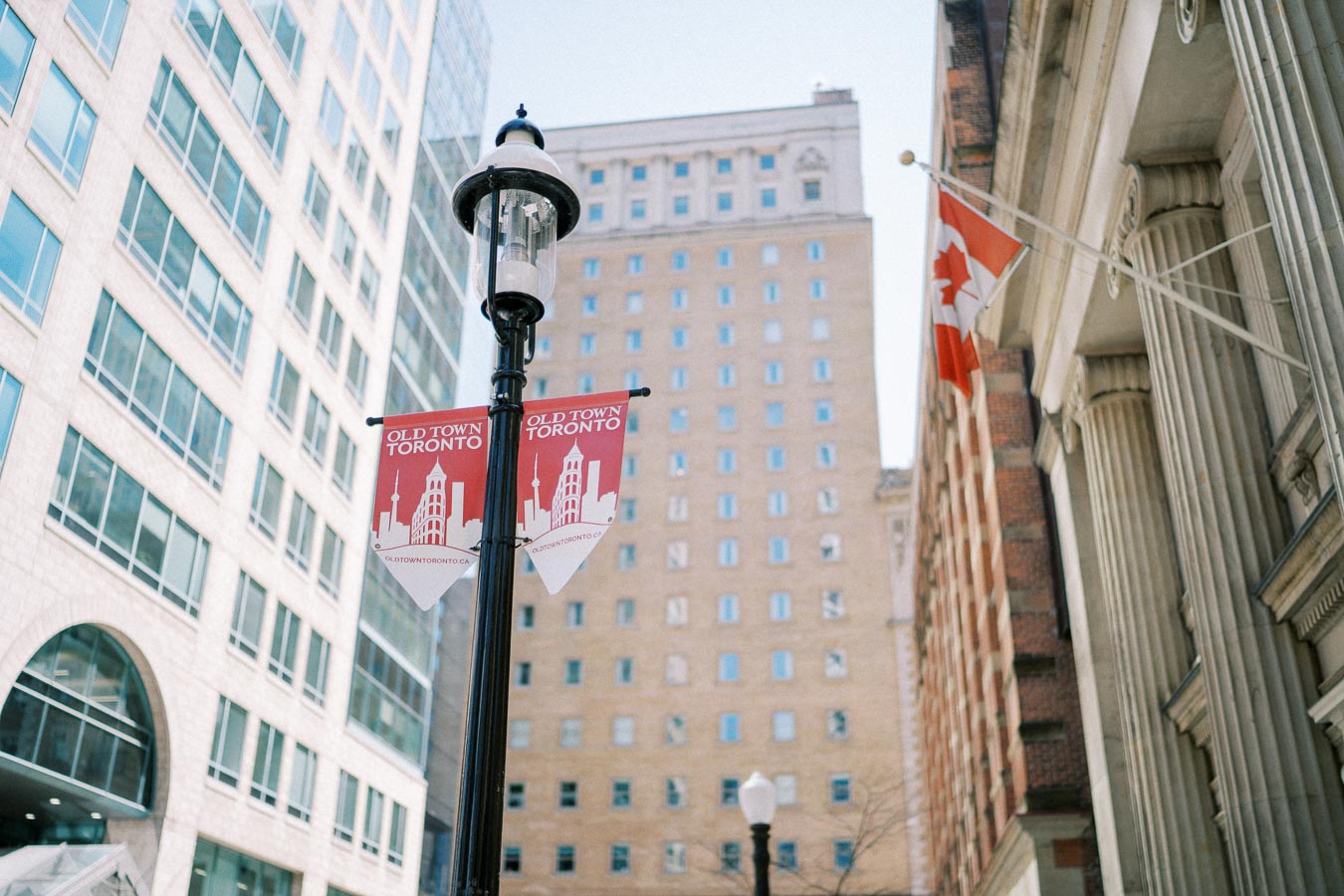 Street view of Old Town Toronto featuring a lamp post with banners, tall modern and historic buildings, and a Canadian flag, showcasing the architectural blend of the area.