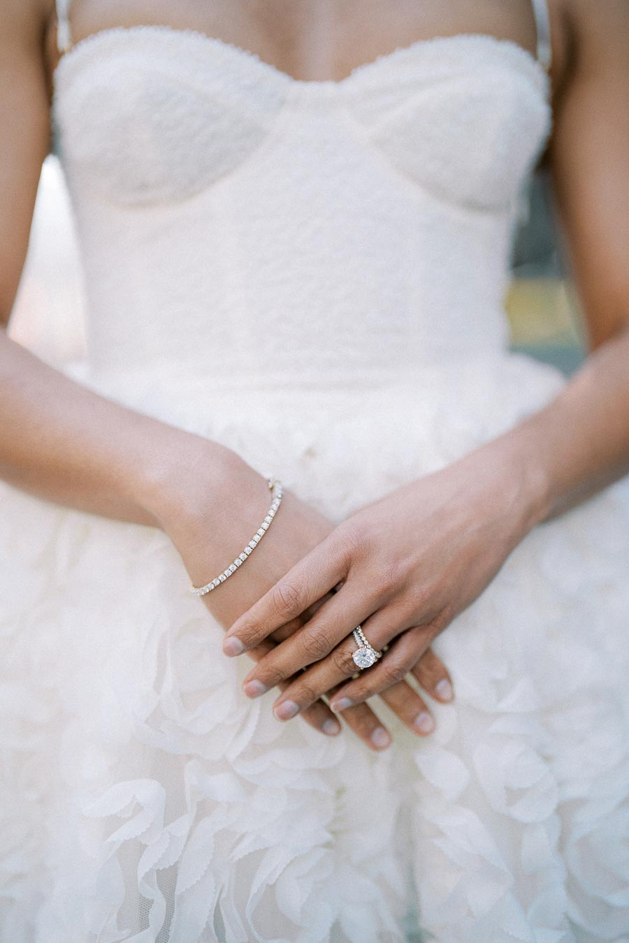 Bride wearing a white strapless wedding dress with lace details, showcasing a diamond bracelet and engagement ring.