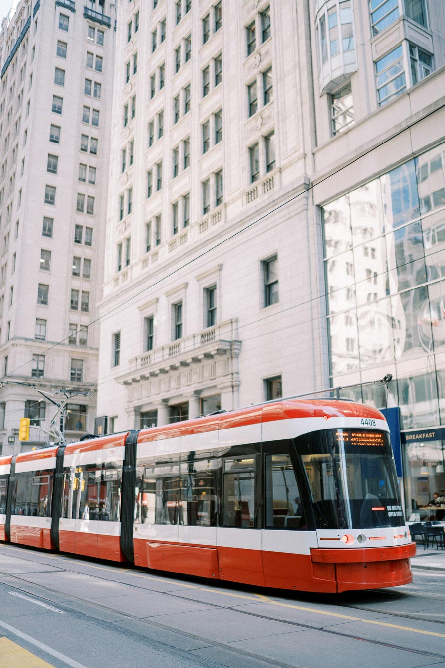 Modern red and white streetcar traveling through a city with tall historic buildings in the background, showcasing urban public transportation in a metropolitan area.