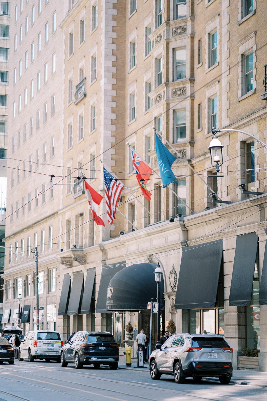 Historic urban hotel exterior with international flags displayed, featuring street view of downtown traffic and pedestrians.