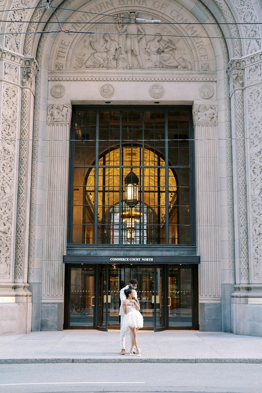 Couple embracing in front of the historic Commerce Court North building entrance, featuring ornate architectural details, in downtown Toronto.