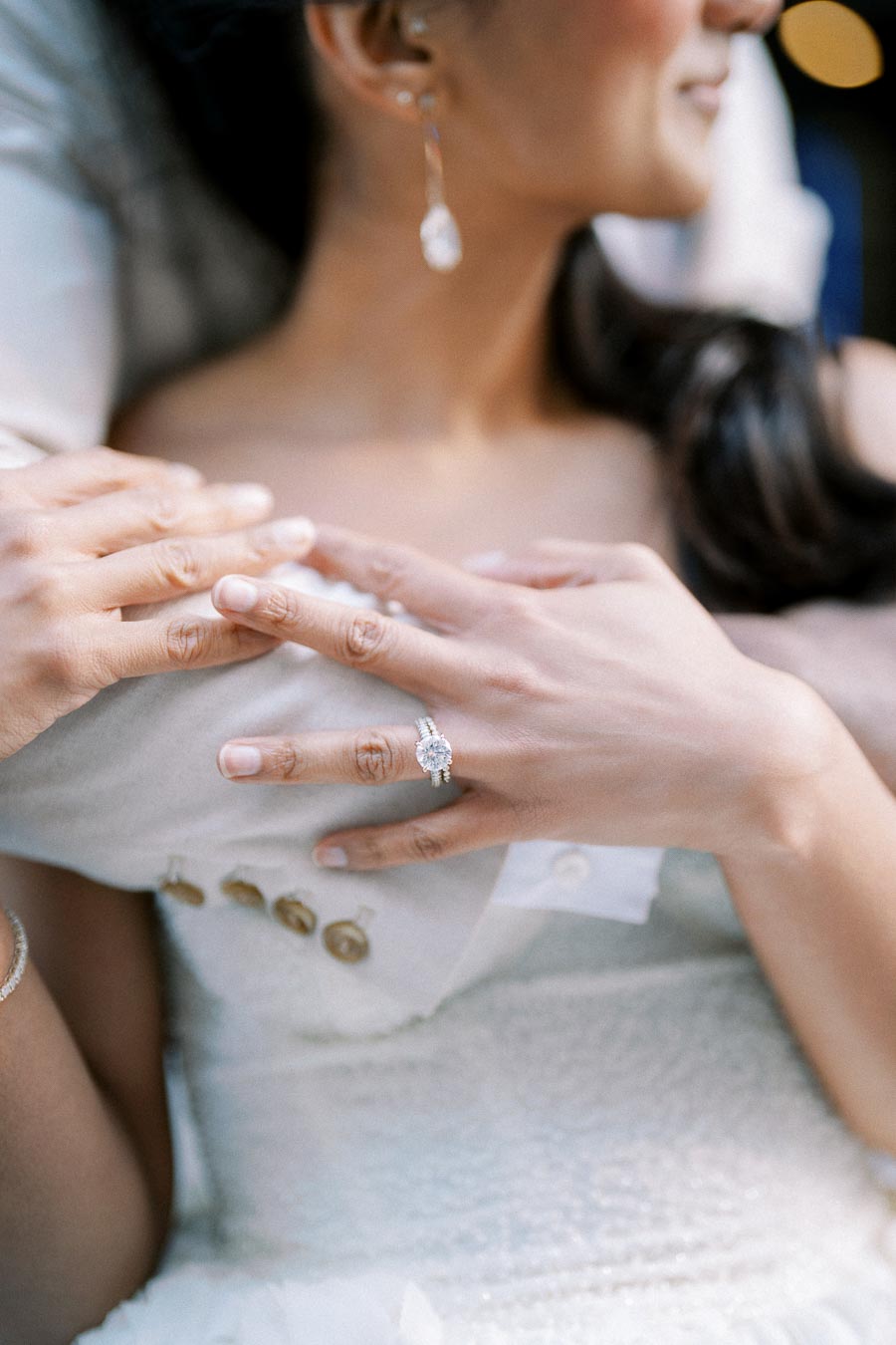 Bride showcasing an elegant diamond engagement ring while embracing her partner, highlighting a romantic moment in wedding attire.