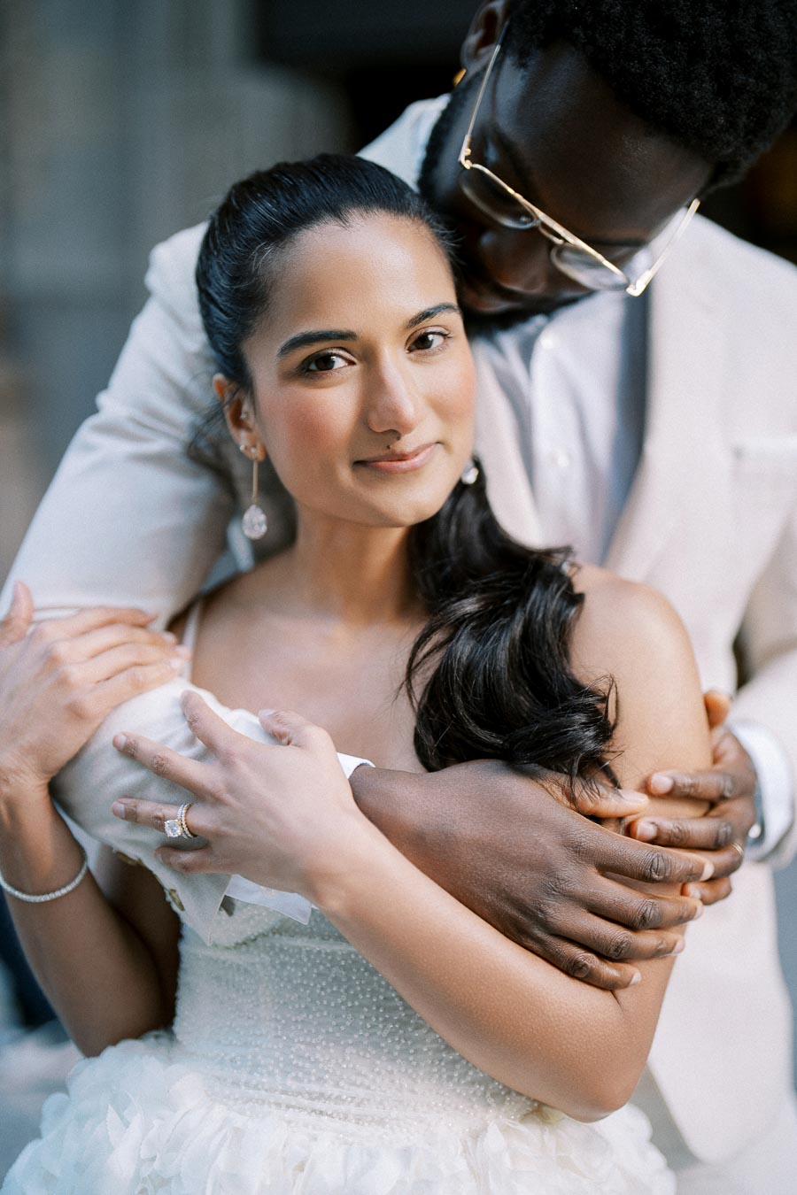 Interracial couple in embracing pose, featuring a woman in a white bridal dress and a man in a light suit, demonstrating love and diversity in wedding photography.