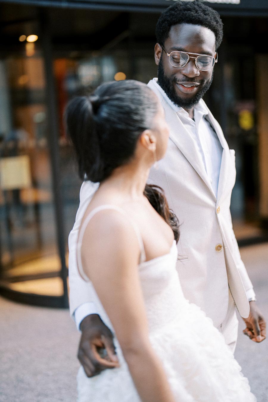 Elegant couple sharing a joyful moment in stylish wedding attire, featuring a man in a light suit and a woman in a white dress, capturing a candid expression of happiness.