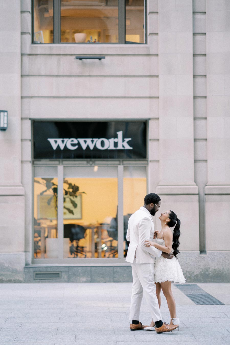 A couple in elegant attire shares a romantic moment outside a WeWork office building.