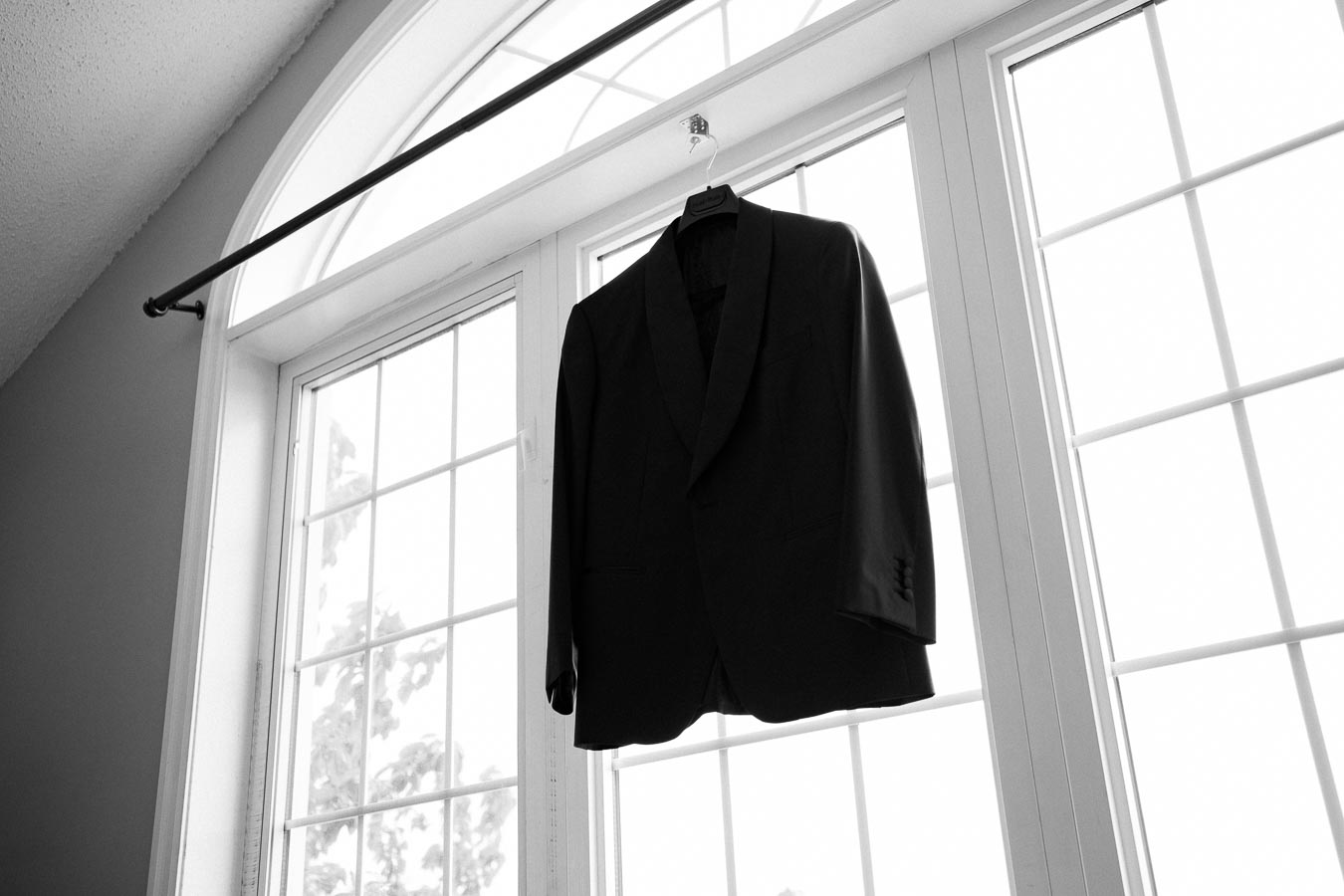 A black suit jacket hanging on a hanger in front of a large arched window, creating a silhouette against the bright natural light.