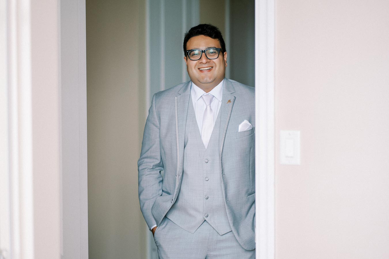 Man in a light gray suit and tie smiling while standing in a doorway