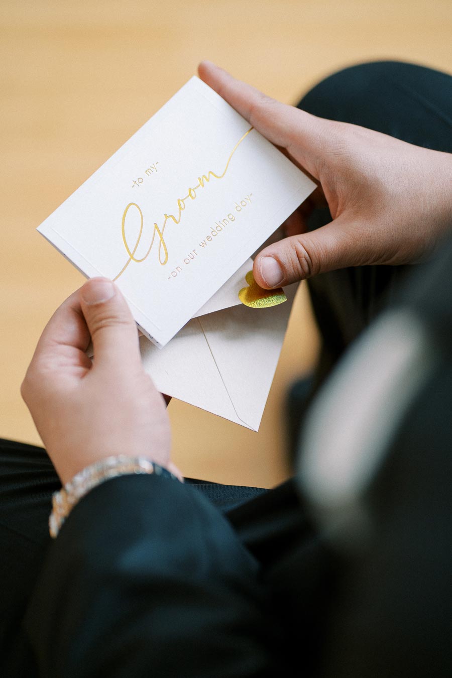 A person holding a wedding card with to my Groom on our wedding day written in elegant gold lettering, symbolizing love and celebration.