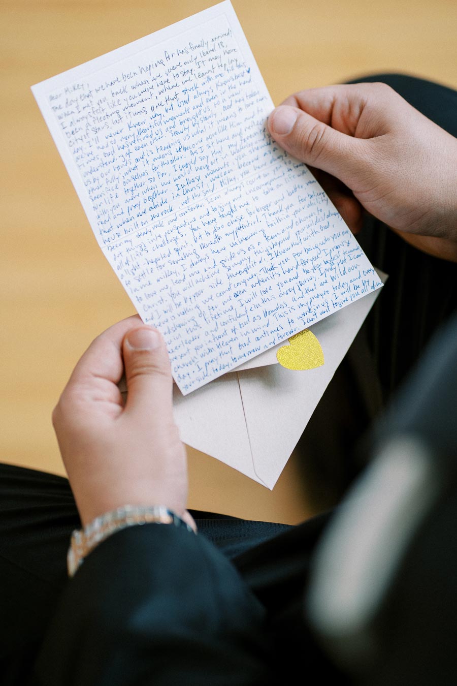 A person holding a handwritten letter with blue ink, partially covering a beige envelope featuring a small yellow heart sticker. The scene captures an intimate moment, highlighting the personal connection and emotion in receiving a letter. Perfect for themes related to communication, relationships, and nostalgia.