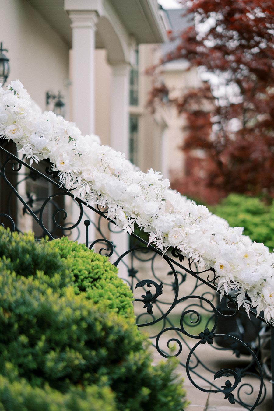 Elegant staircase adorned with lush white floral arrangements, featuring intricate wrought iron railings and lush greenery, creating a sophisticated and serene atmosphere.