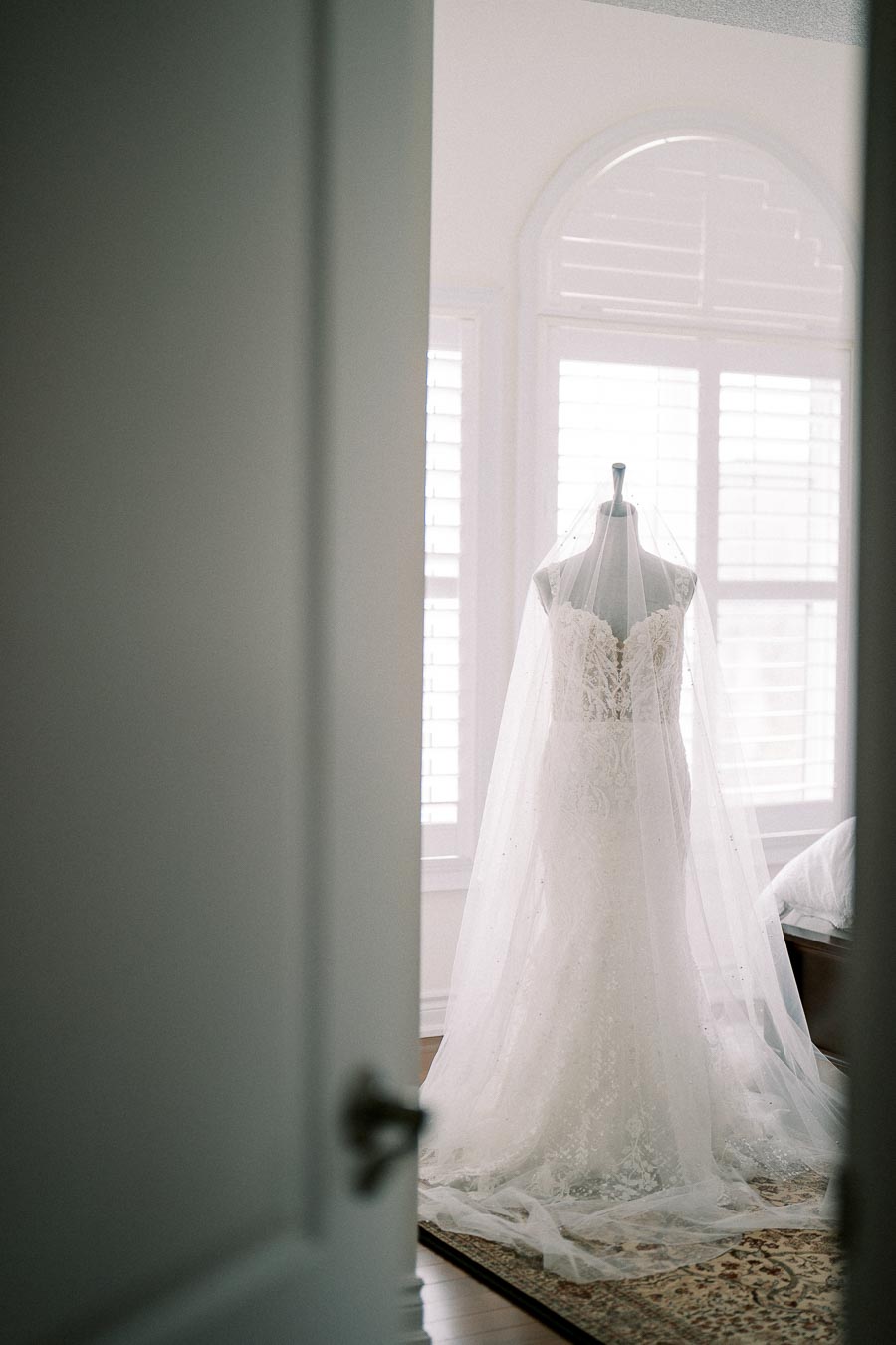 Bridal gown on display in a well-lit room, featuring intricate lace details and a long veil, perfect for a classic wedding.