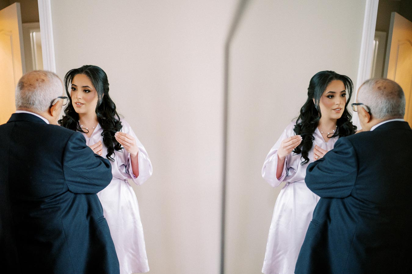 A bride in a satin robe talks with an elderly man, reflecting in the mirror.