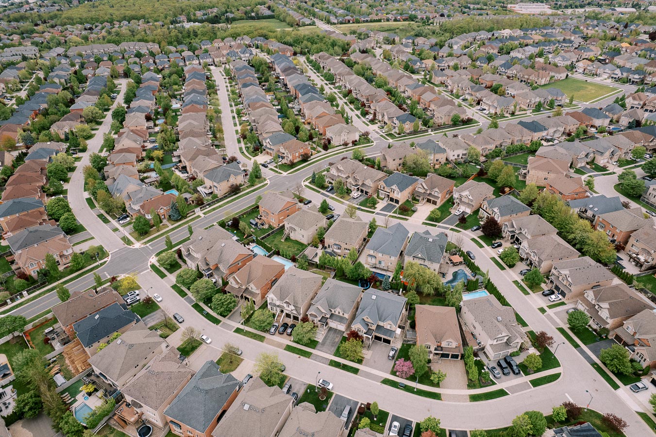 Aerial view of a suburban neighborhood with rows of houses, tree-lined streets, and well-maintained lawns, showcasing a planned community layout.