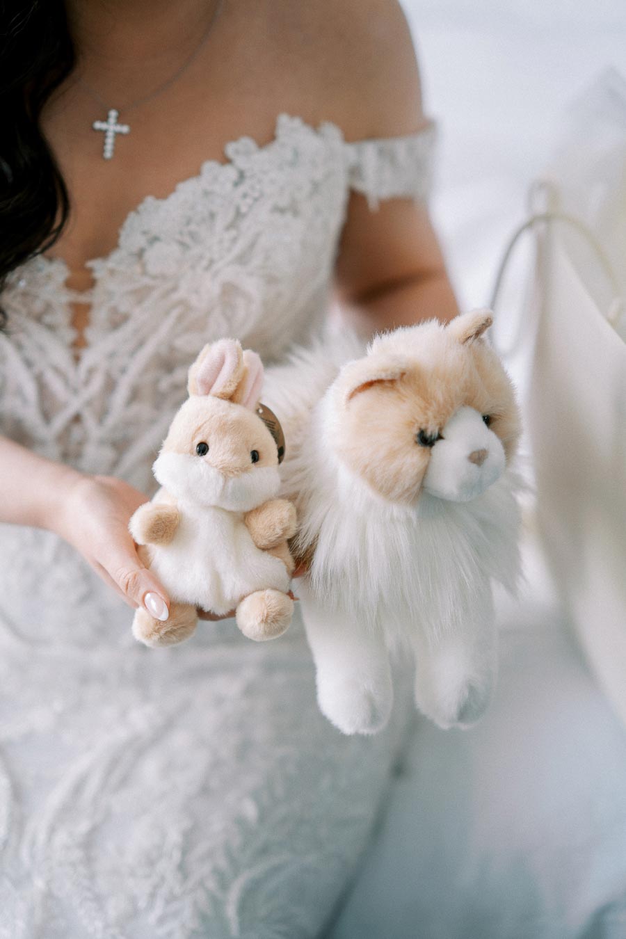 A bride in a lace wedding dress holding plush toys of a bunny and a cat, showcasing delicate bridal details and a playful touch.