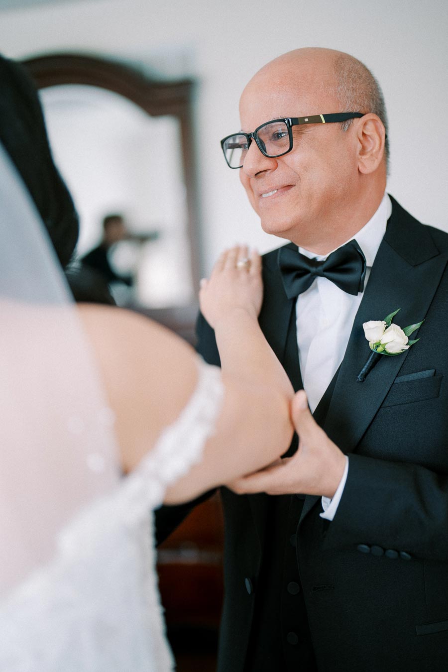 Father of the bride in a tuxedo smiling as he holds his daughter's hand on her wedding day.