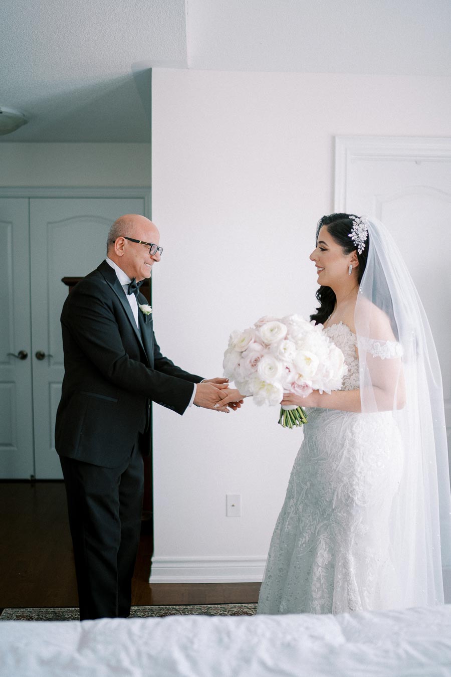Bride and father sharing a joyful moment before the wedding ceremony, with the bride holding a bouquet of white flowers in an elegant room.