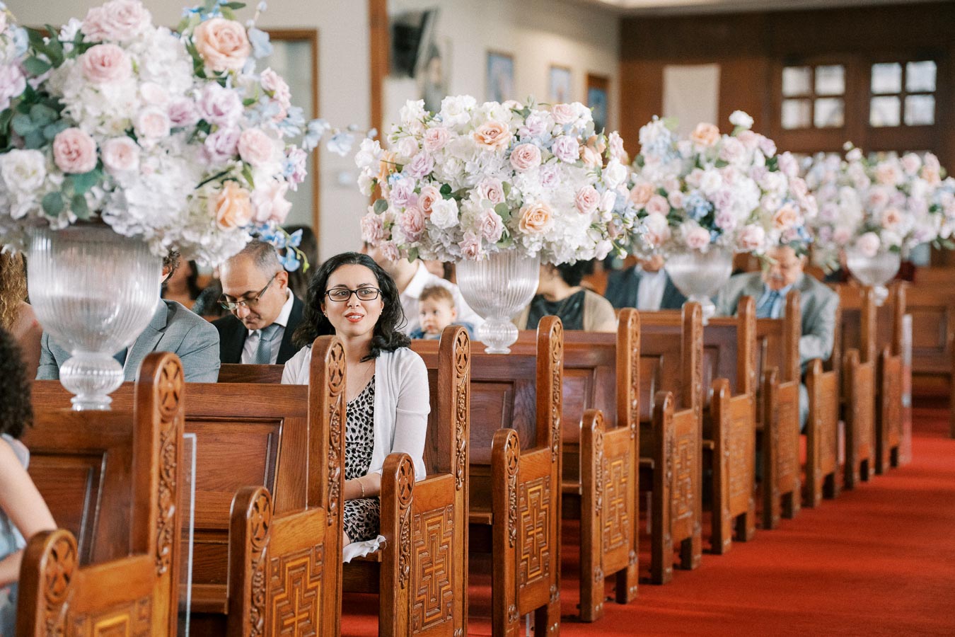 Guests seated in a church, decorated with large pastel flower arrangements.