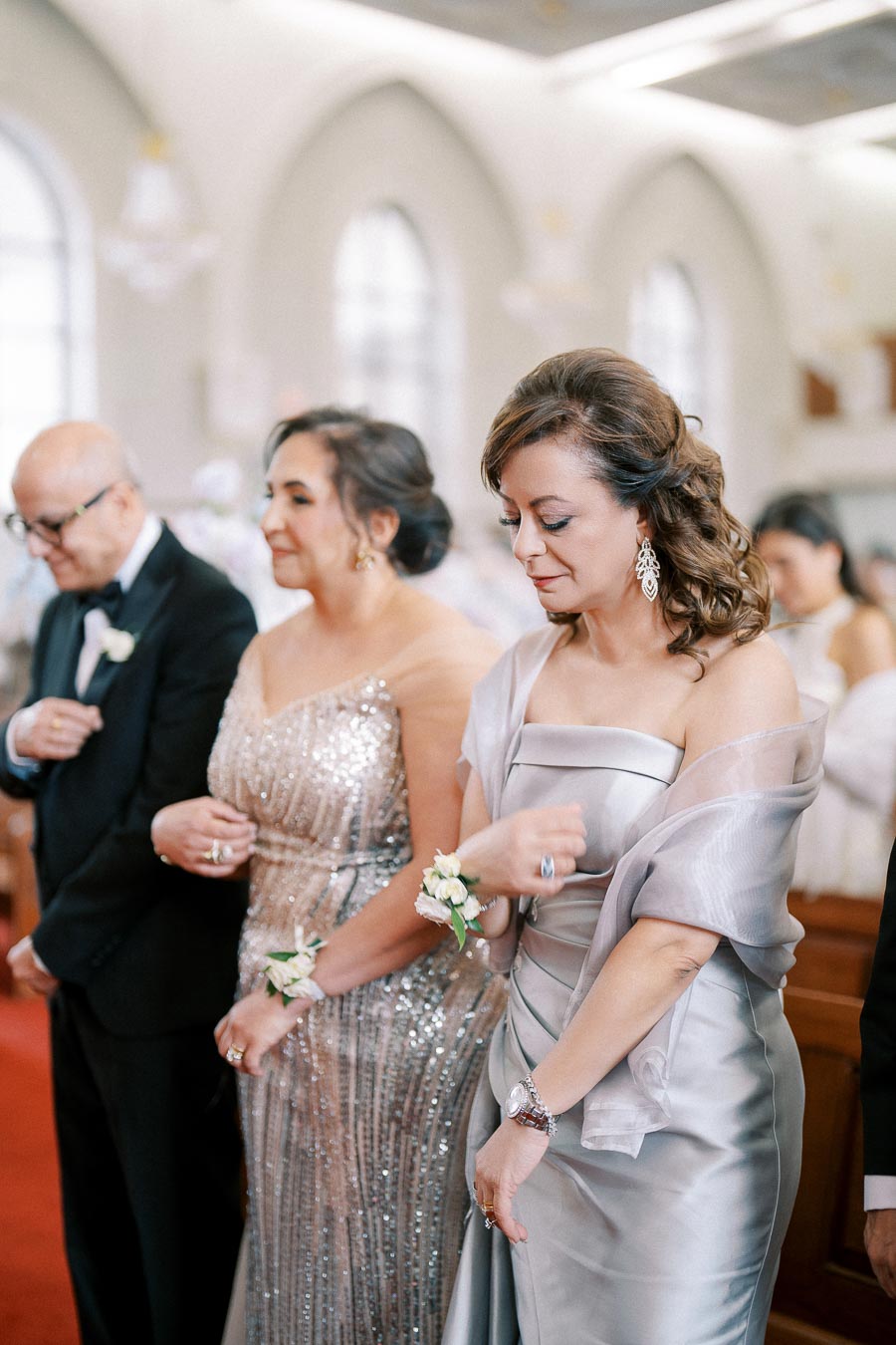 Elegant wedding guests dressed in formal attire, standing inside a beautifully decorated church with soft natural lighting.