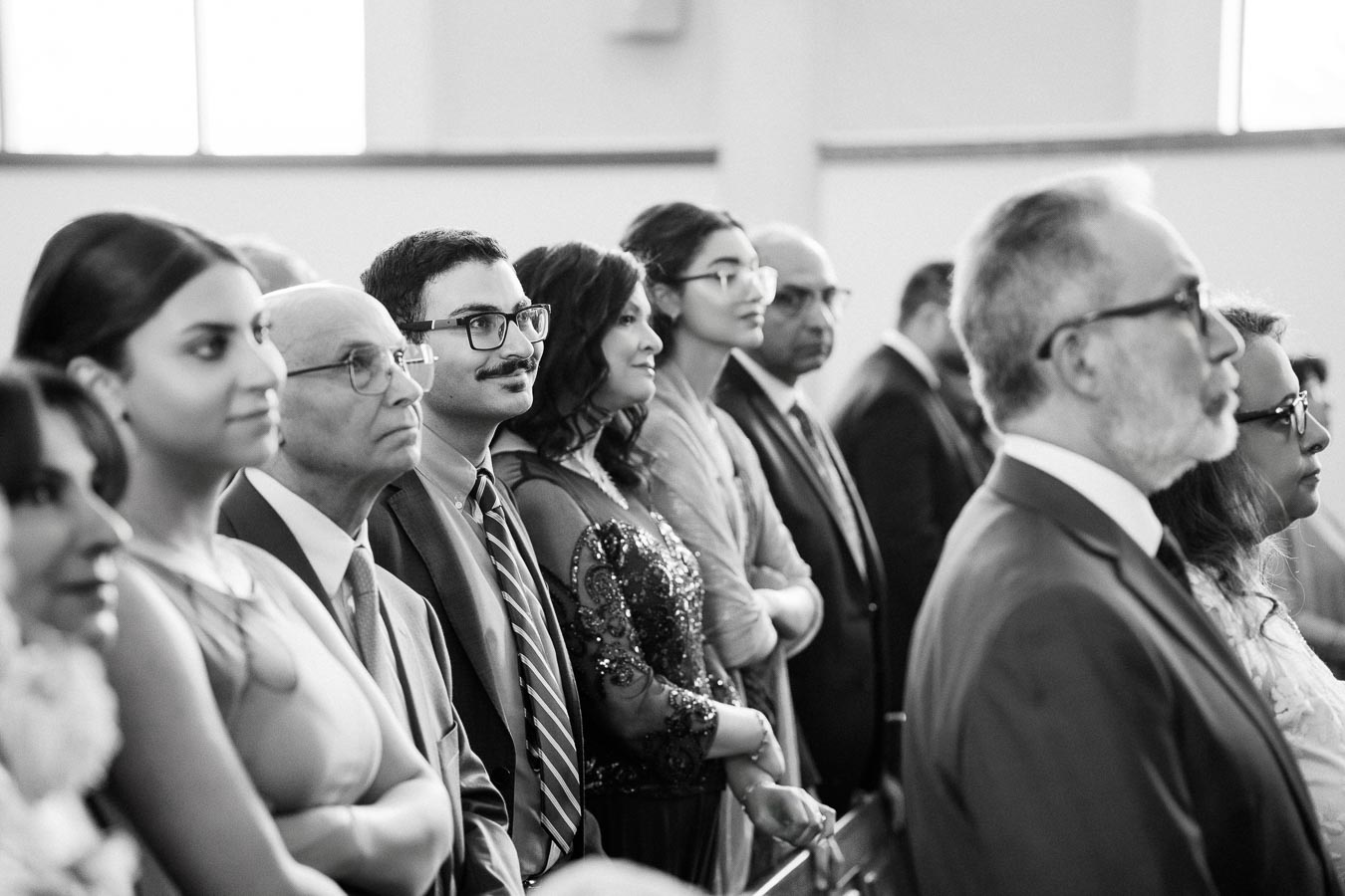 A group of well-dressed people attentively watching a ceremony inside a bright room.