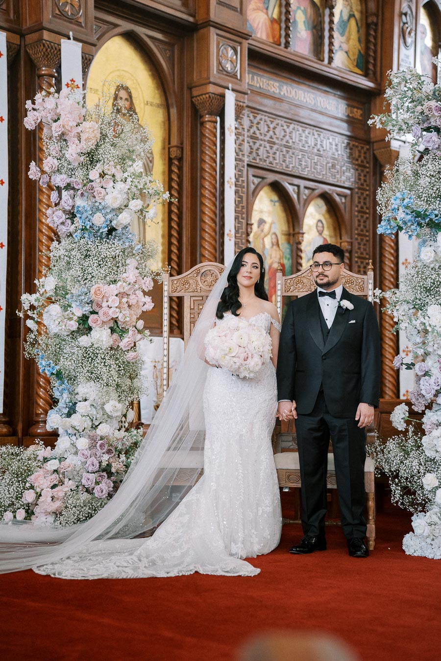 Bride and groom standing together in a beautifully decorated church, surrounded by floral arrangements and intricate woodwork, capturing a moment of their wedding ceremony.