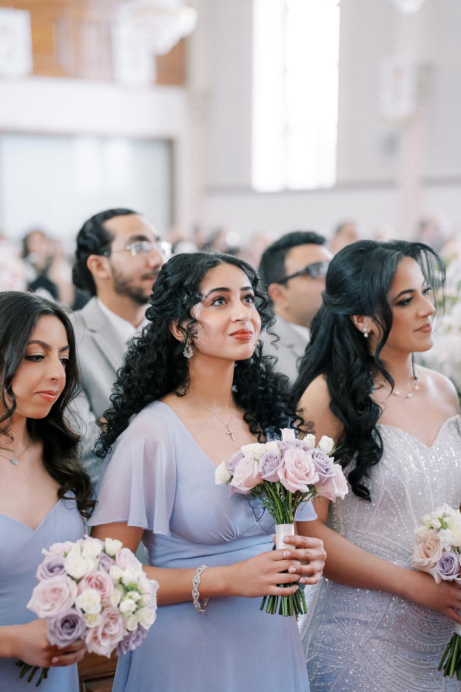 Bridesmaids in lavender dresses holding pastel bouquets at a wedding ceremony.