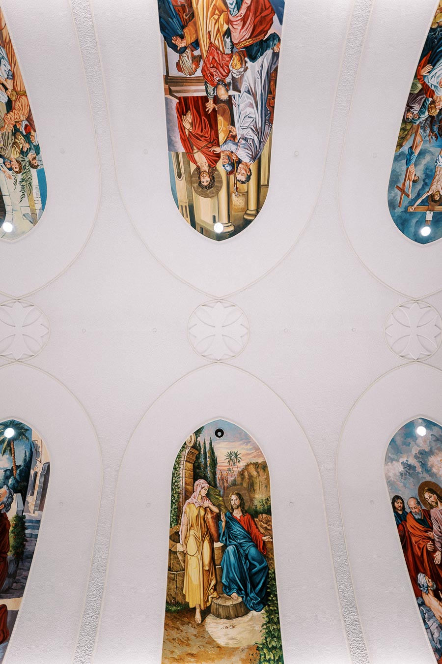 Ceiling of a church with detailed religious frescoes, depicting biblical scenes and figures in a series of arched panels, creating a serene and sacred atmosphere.
