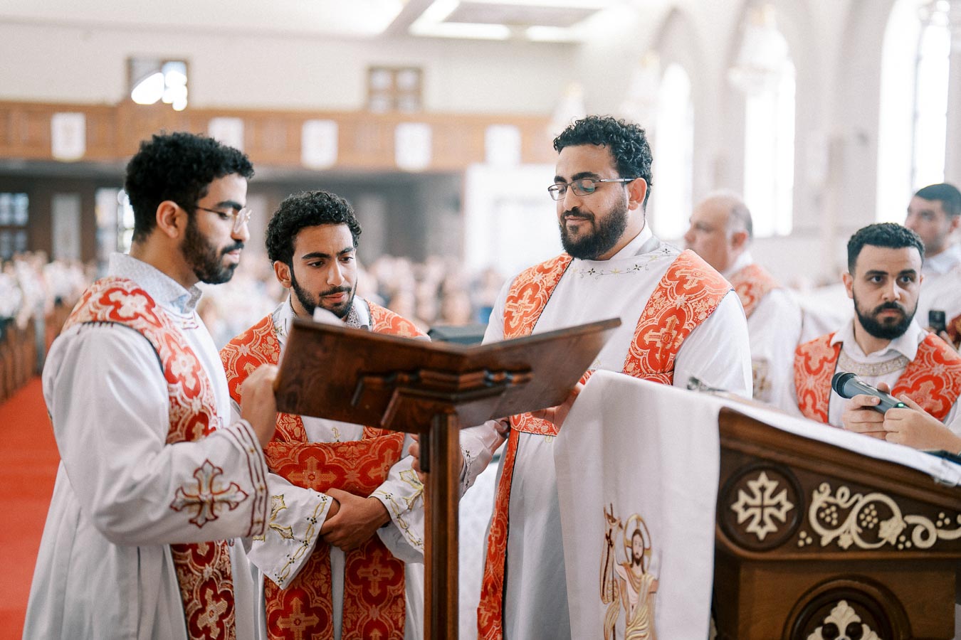 A group of clergy in traditional red and white vestments standing around a wooden lectern during a church service.
