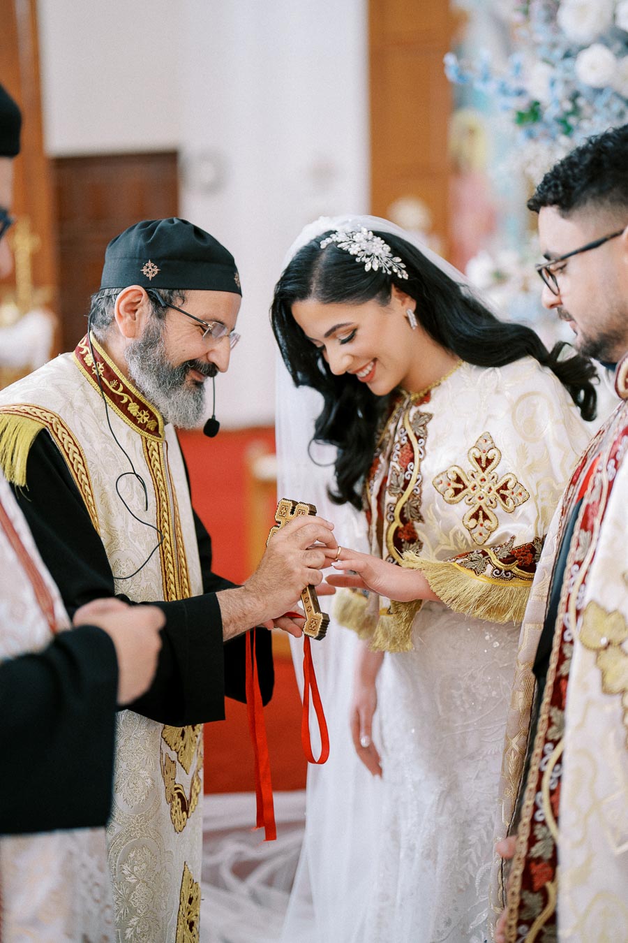 Wedding ceremony with priest and bride exchanging rings in a traditional setting, adorned in intricate embroidered garments.