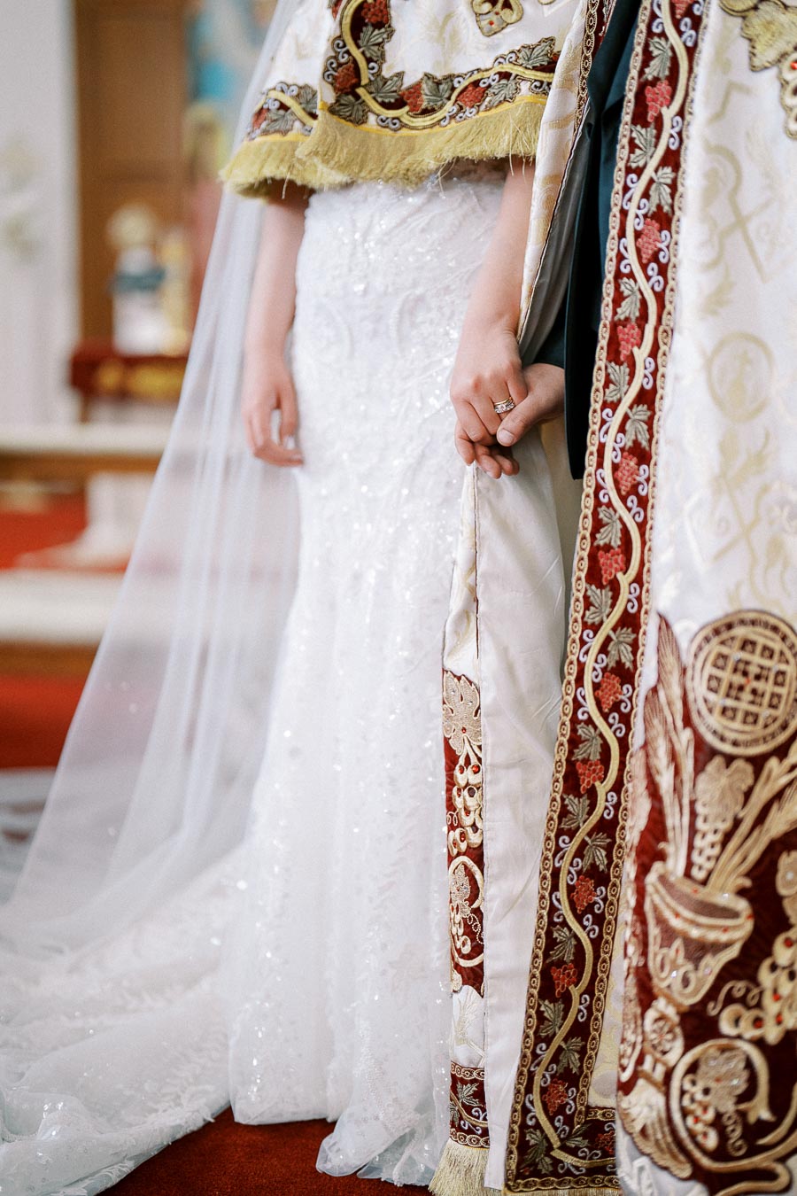 A bride and another person holding hands during a wedding ceremony, showcasing intricate, embroidered traditional garments and a white wedding dress, emphasizing cultural and ceremonial elegance.
