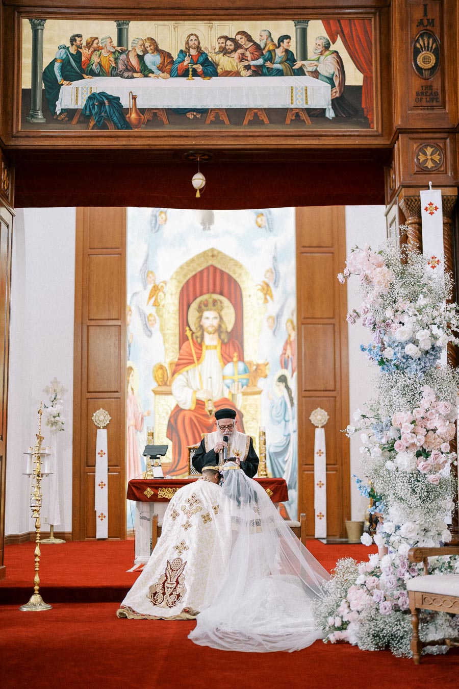 A priest conducting a traditional wedding ceremony in a richly decorated church interior, featuring religious artwork and intricate floral arrangements.