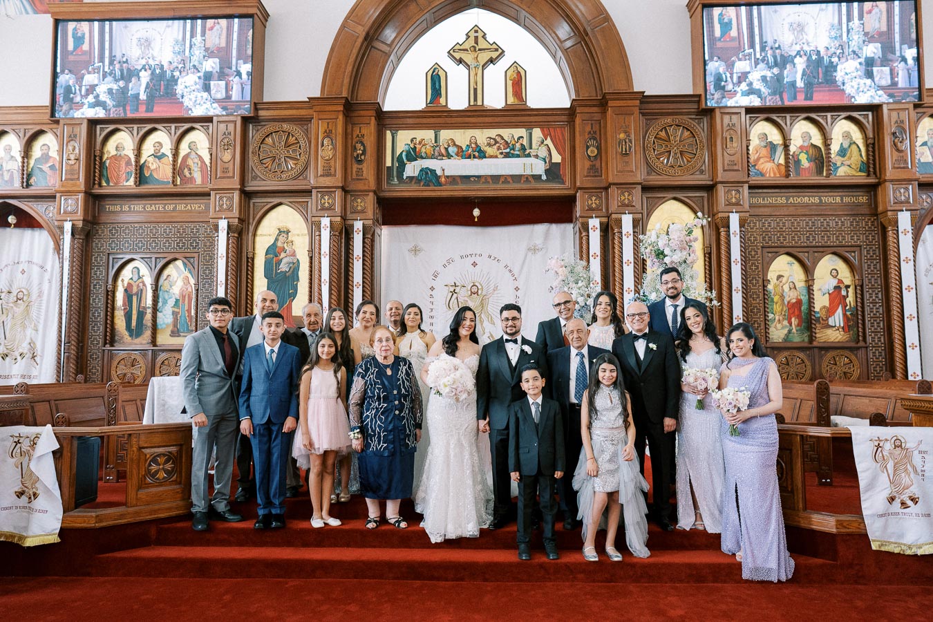 A large family posing for a wedding photo inside a beautifully decorated church with ornate wooden panels and religious iconography.