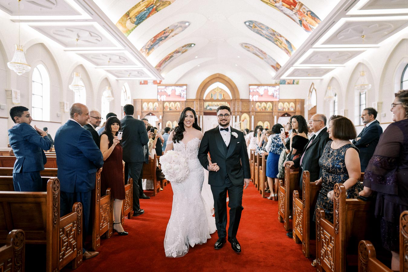 Bride and groom walking down the aisle in a beautifully decorated church, surrounded by smiling guests, capturing a joyful wedding moment.