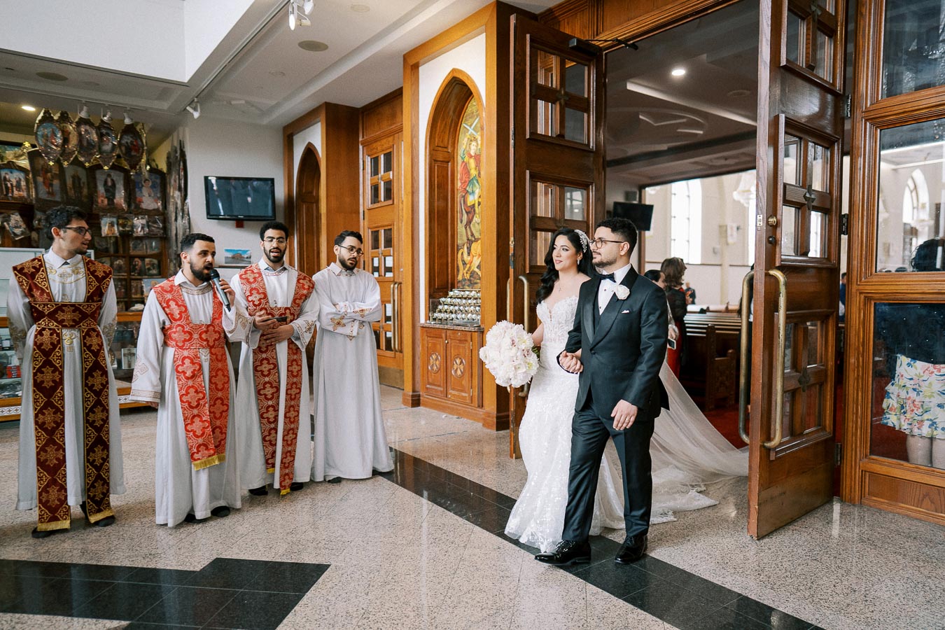 A bride and groom walking down the aisle in a church, surrounded by priests in ceremonial robes, emphasizing a traditional wedding procession.