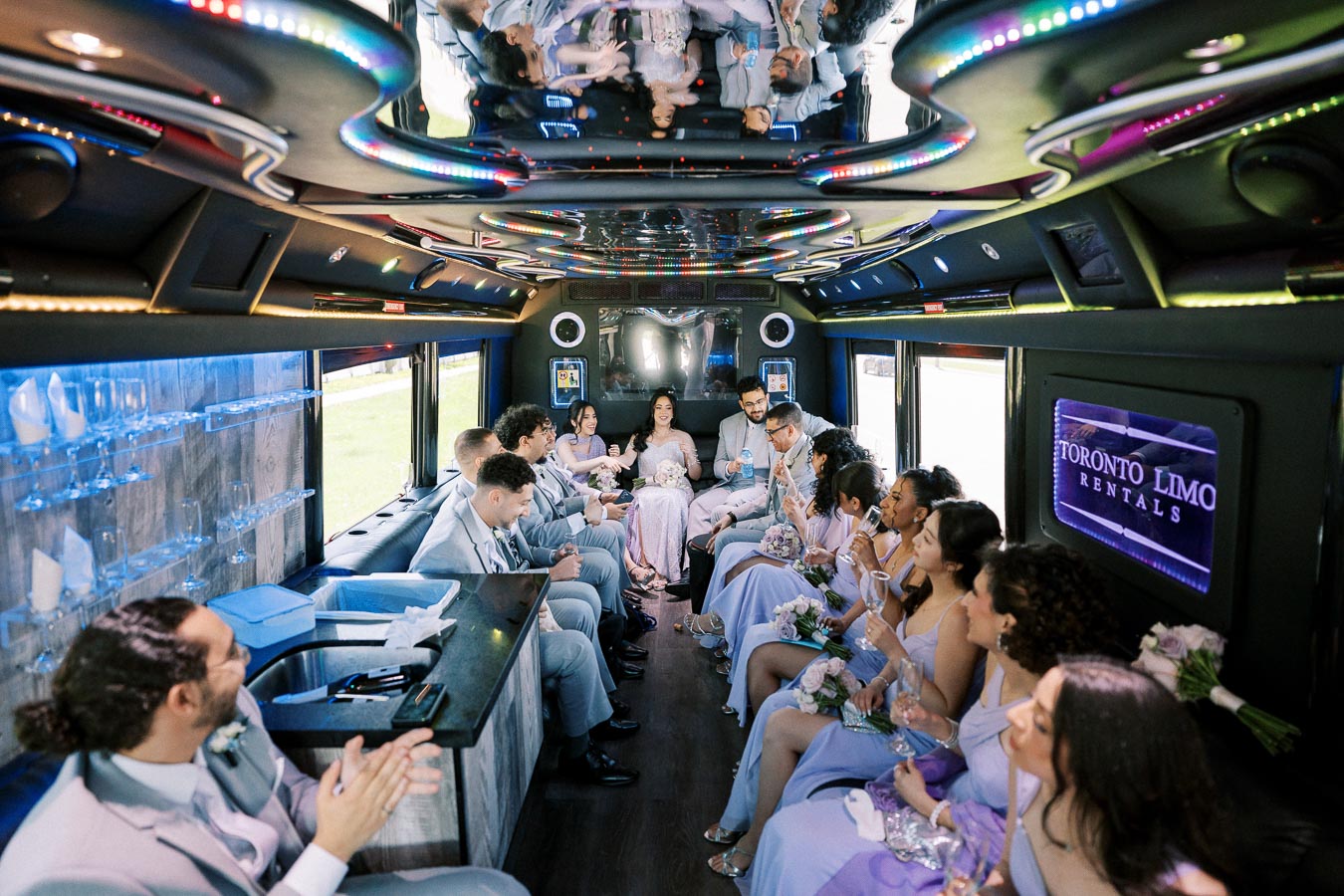 A wedding party enjoying a lavish ride inside a luxury limo bus by Toronto Limo Rentals. The elegantly dressed group, seated comfortably, is surrounded by ambient lighting and sleek interior features, perfect for a stylish celebration.