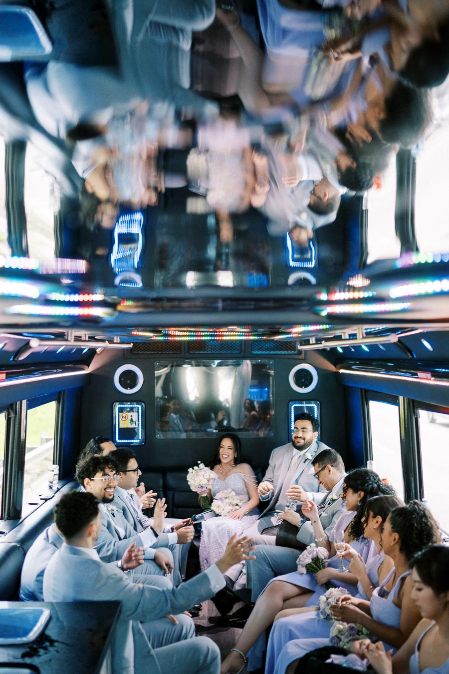 Wedding party celebrating inside a decorated limo, featuring a joyful bride holding a bouquet and guests in elegant attire, with colorful lighting creating a festive atmosphere.
