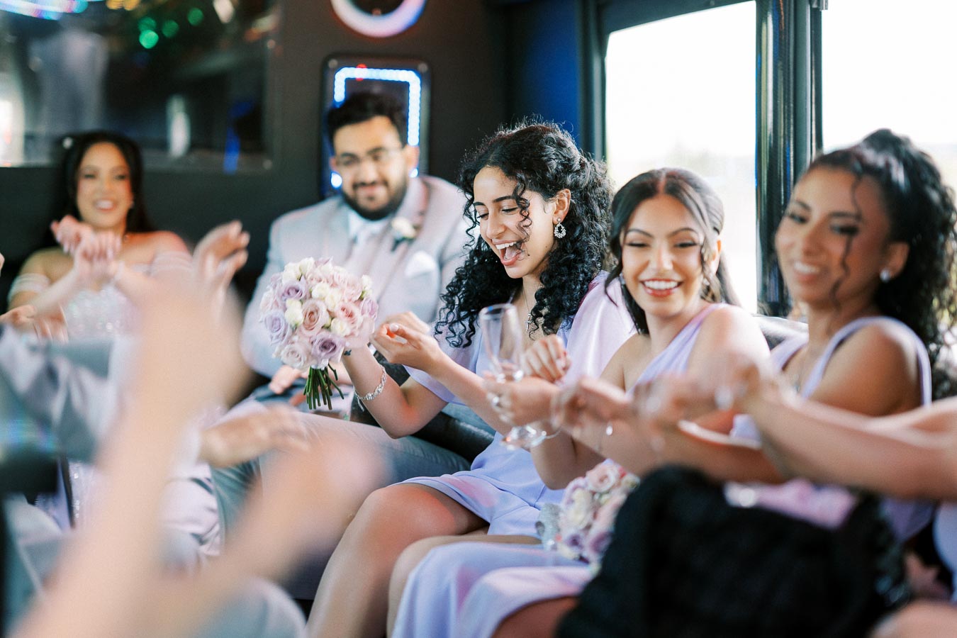 Group of people celebrating inside a limo, with a woman holding a bouquet of pastel-colored flowers; joyful and festive atmosphere at a wedding or special event.