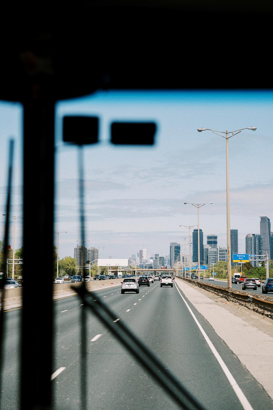 Highway view with cars heading towards a city skyline in the distance, featuring tall skyscrapers under a clear blue sky.