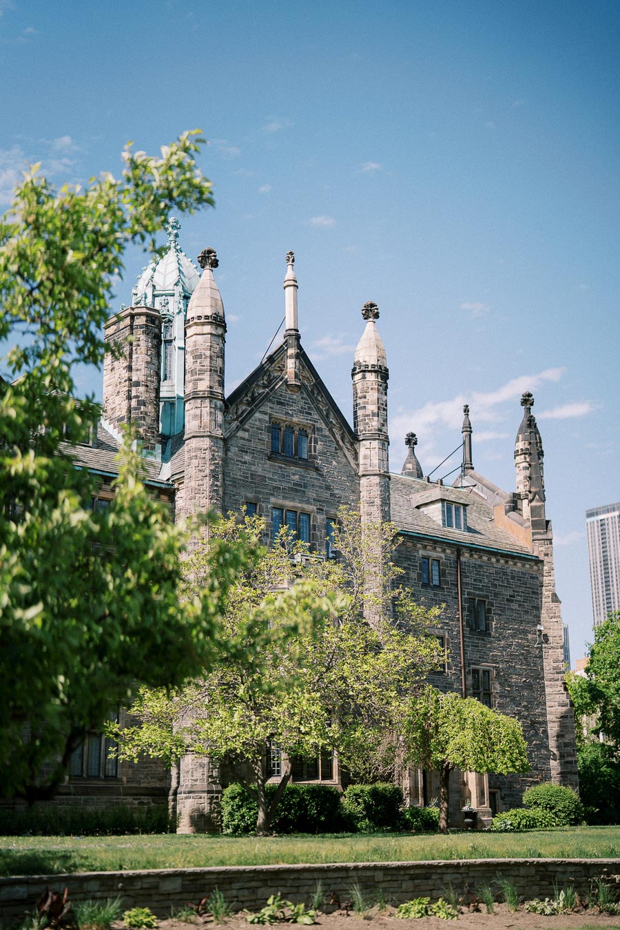 Historic stone building with ornate spires surrounded by lush greenery under a clear blue sky.