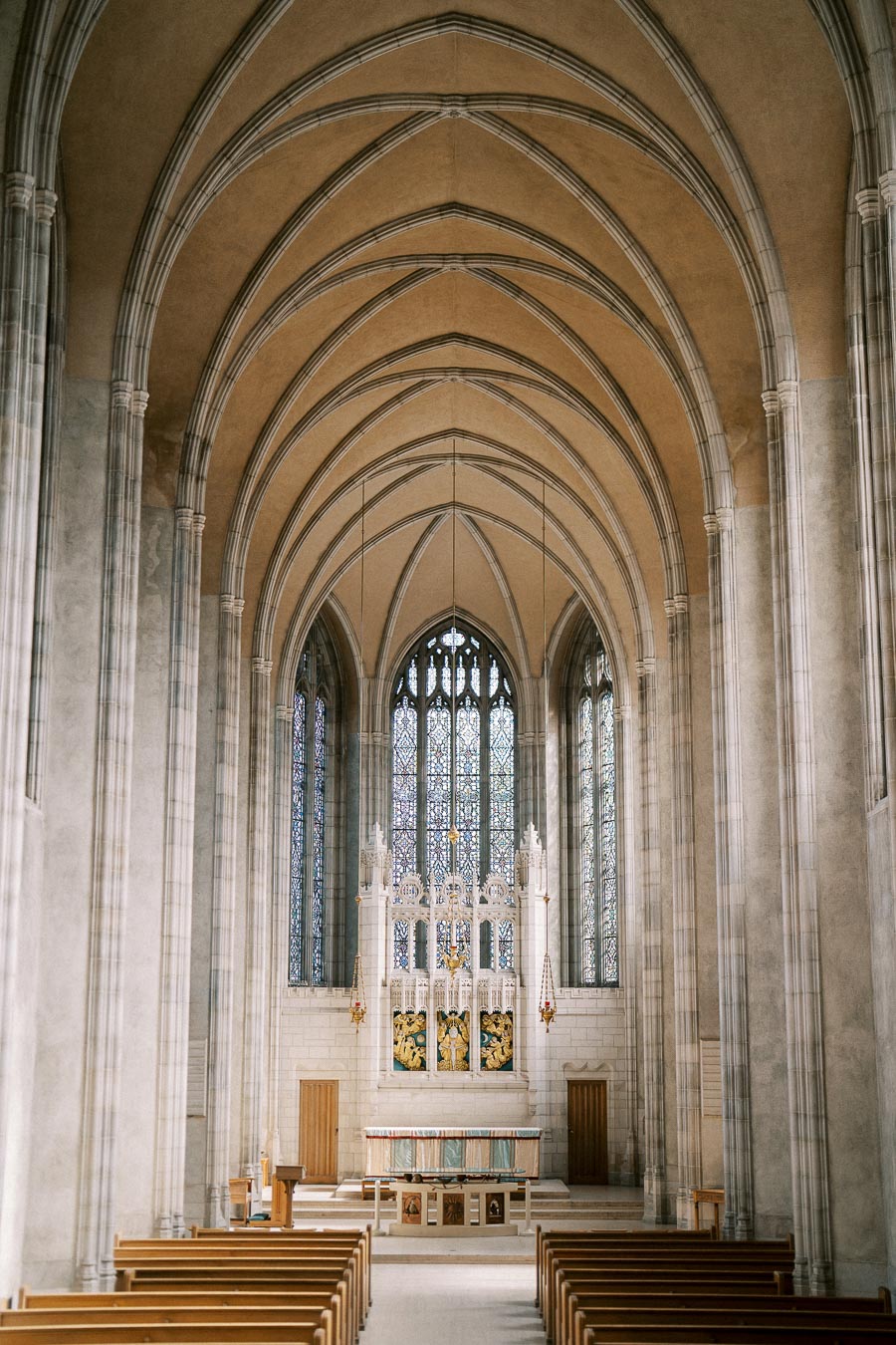 Alt text: Interior of a Gothic-style church showcasing high vaulted ceilings, intricate stained glass windows, and wooden pews leading to a decorated altar.
