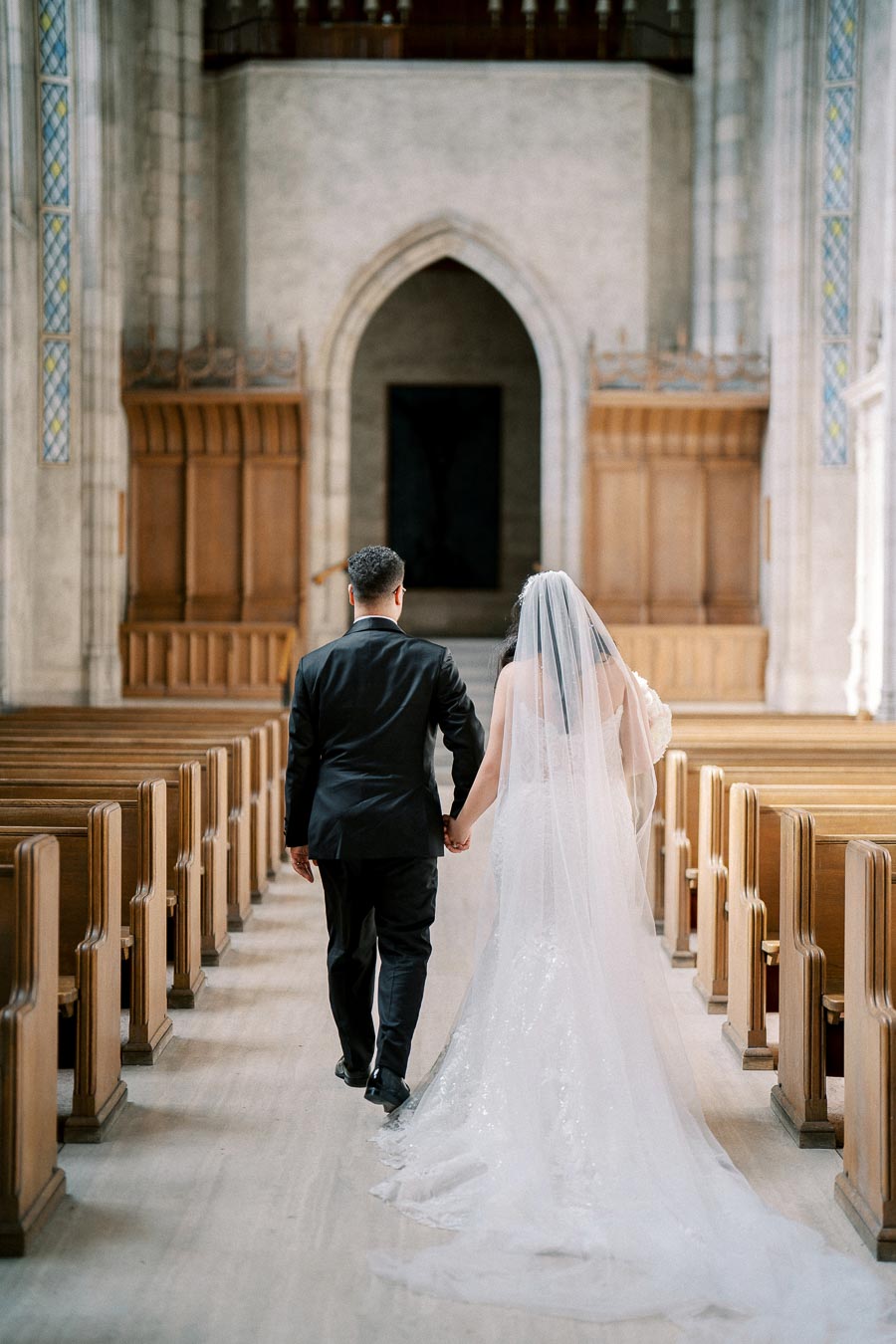 Wedding couple walking down the aisle in a beautiful church, bride in elegant white gown and veil, and groom in a black suit, symbolizing love and commitment.