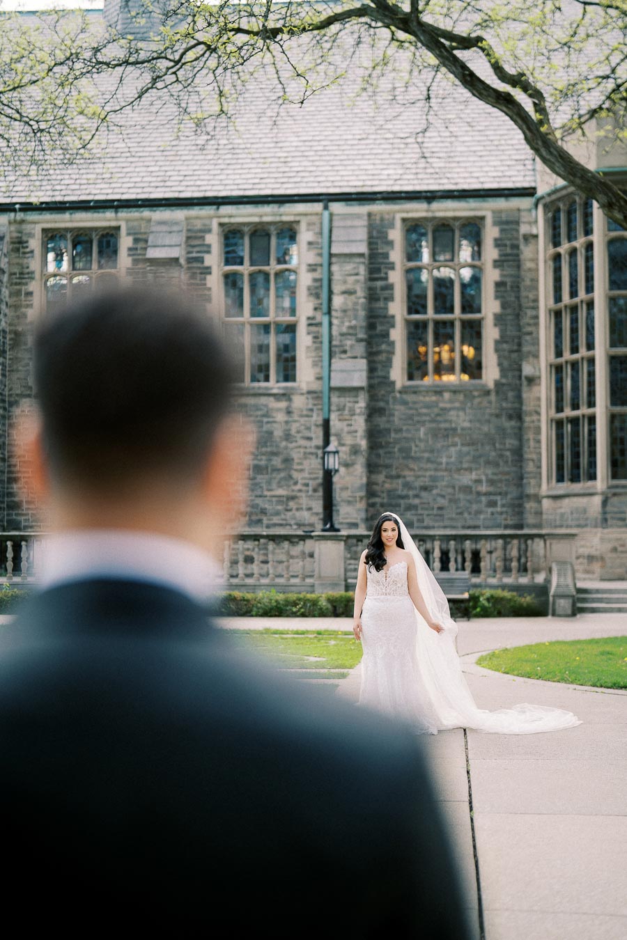Bride in a white wedding dress walking towards groom at historic stone building.