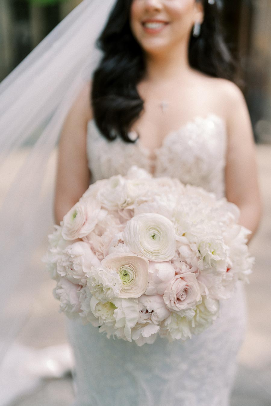 Bride wearing a lace wedding gown holding a large bouquet of white and blush flowers.