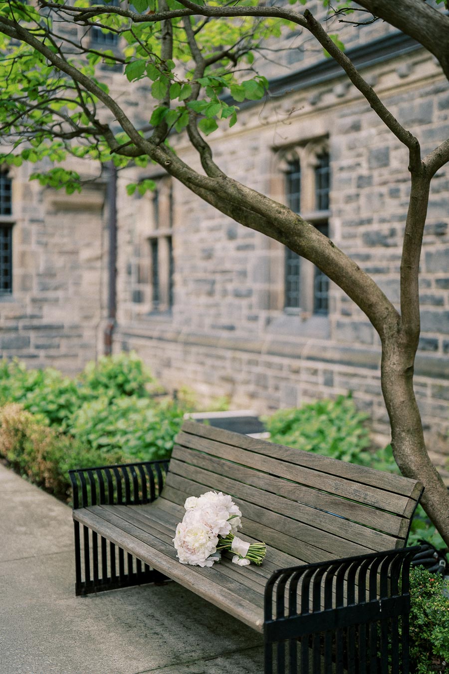 Wooden bench with white flower bouquet under a tree beside a historic stone building