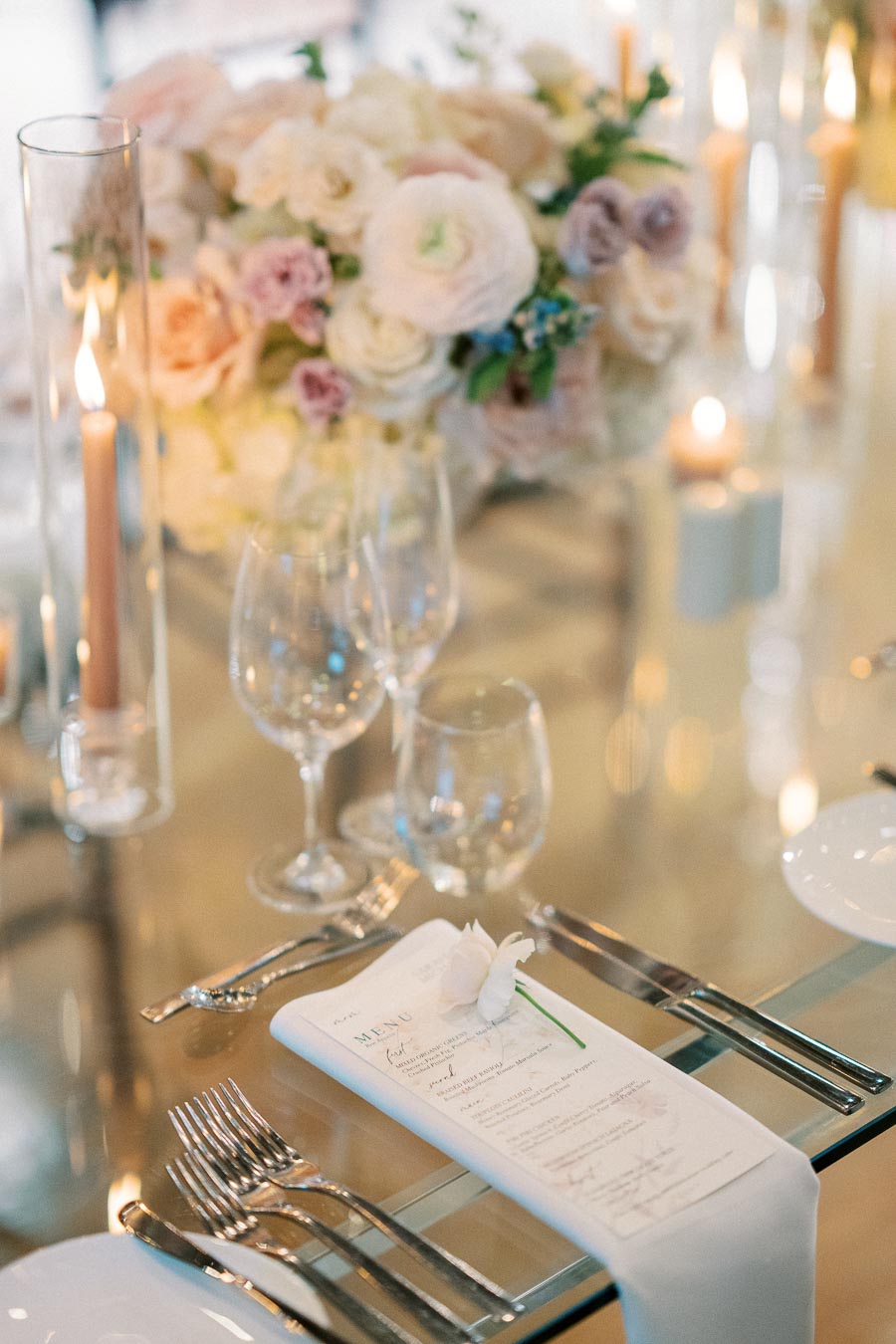 Elegant wedding table setting with a floral centerpiece, candles, wine glasses, and a menu elegantly placed on a napkin, creating a romantic ambiance.