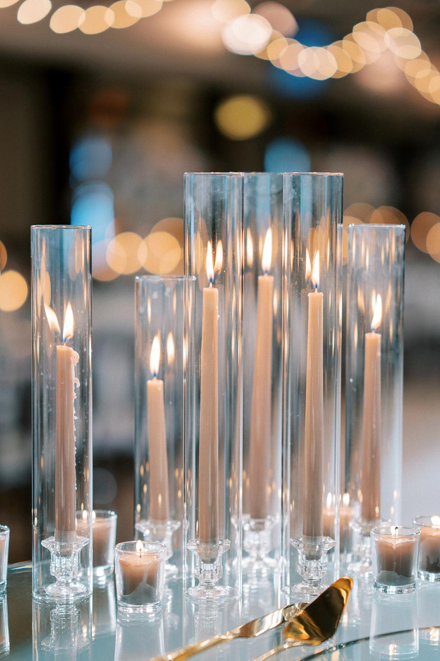 Elegant tall candles in clear glass holders create a warm, romantic ambiance with soft, glowing light reflected on a polished surface, perfect for weddings or intimate gatherings.