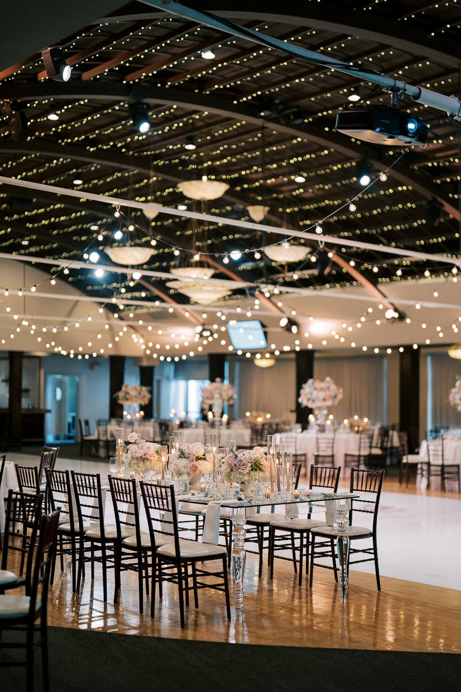Elegant wedding reception venue with beautifully decorated tables, floral centerpieces, and ambient string lighting, creating a romantic and inviting atmosphere.