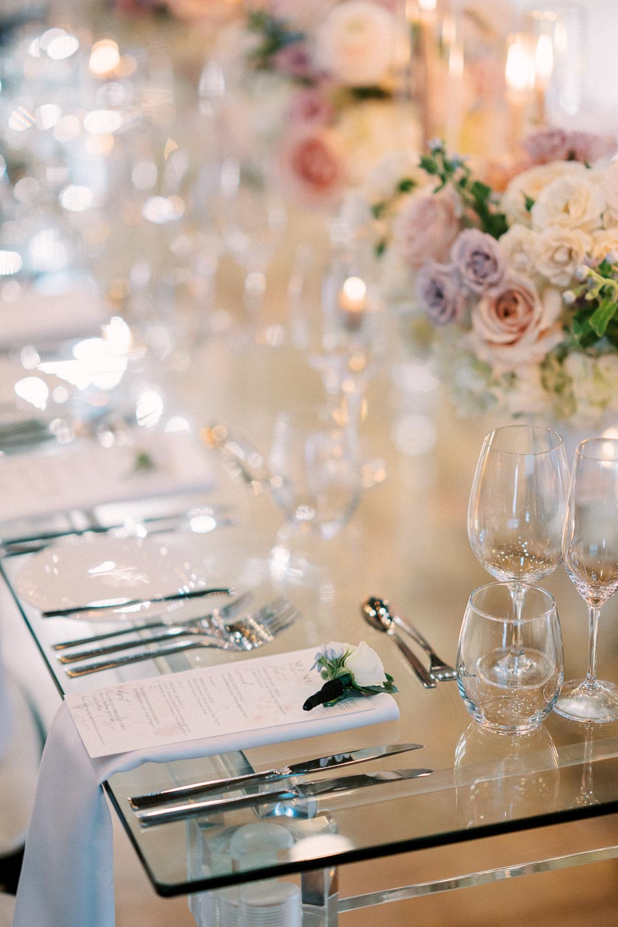 Elegant wedding table setting with crystal glassware, white plates, and floral centerpieces featuring pink and white roses, designed for a sophisticated event ambiance.