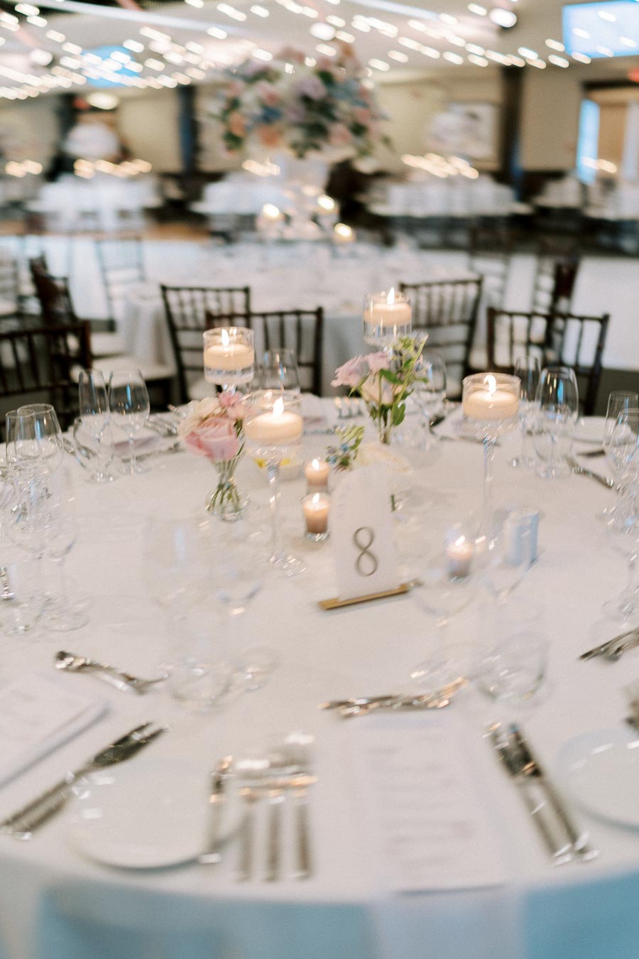 Elegant wedding reception table setting with floral centerpieces, floating candles, and table number eight displayed in a softly lit banquet hall.