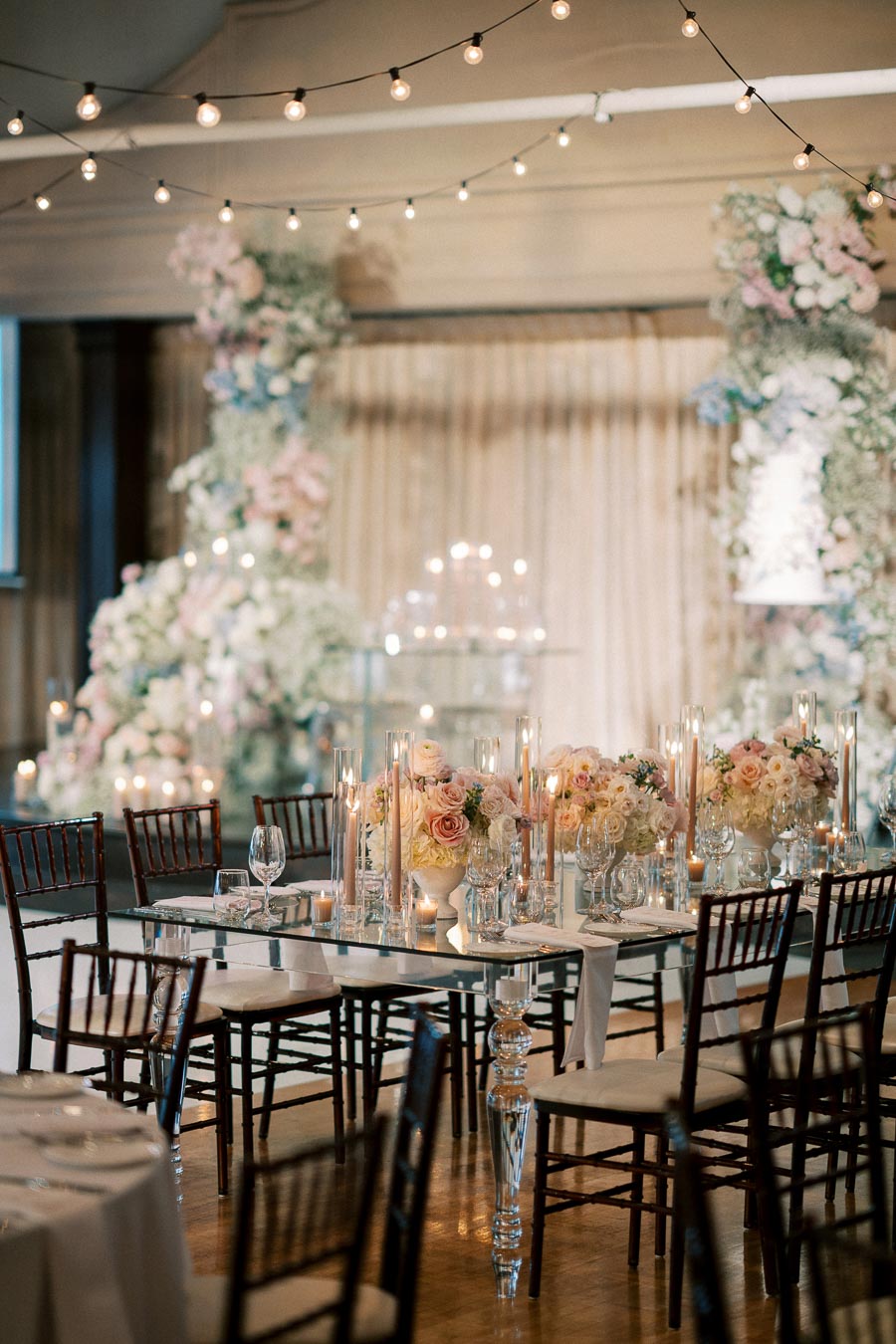 Elegant wedding reception setup with floral centerpieces and string lights, featuring a beautifully arranged table with candles and fine glassware, creating a romantic ambiance.